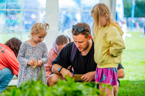 Photo shows a man and two young girls making seed packets in a pavilion