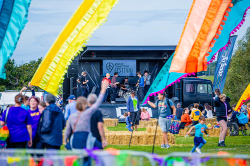 A few of a festival stage showing people sitting on hay bales or up on their feet
